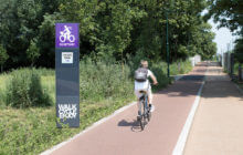 Digital cycle counter totem next to a cycle path & someone riding a bicycle.