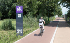 Digital cycle counter totem next to a cycle path & someone riding a bicycle.